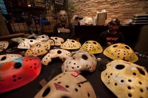 Dee dons a hockey horror mask as Tim Shultz looks on. They sell hand-crafted, hand-painted Jason-style hockey masks at RockeyHorrorMask.com.