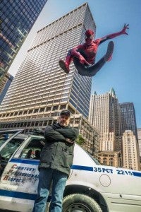 Amazing Spider-Man leaps through the air above a police car in a set photo