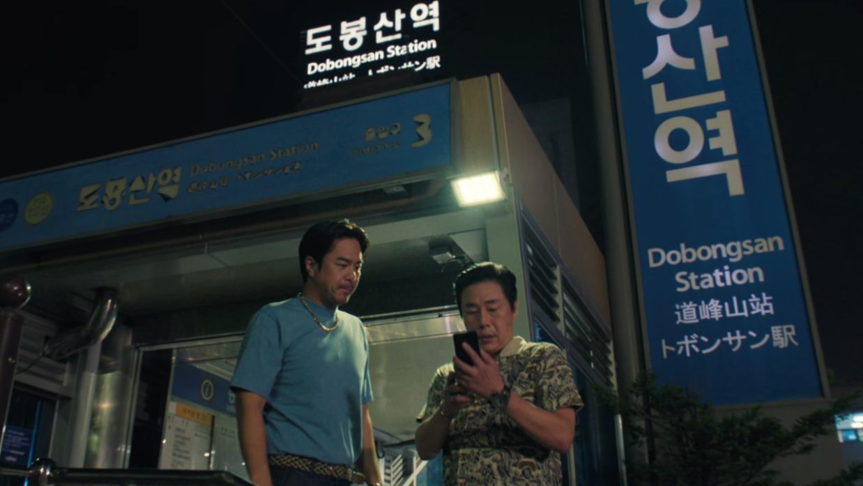 Woo seok with the boss of sunshine capital standing outside a station in episode 1 of squid game 2