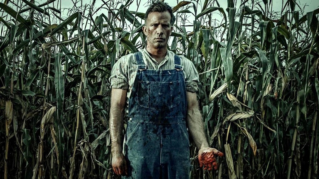 Thomas Jane standing in cornfield wearing overalls and with blood-stained hand