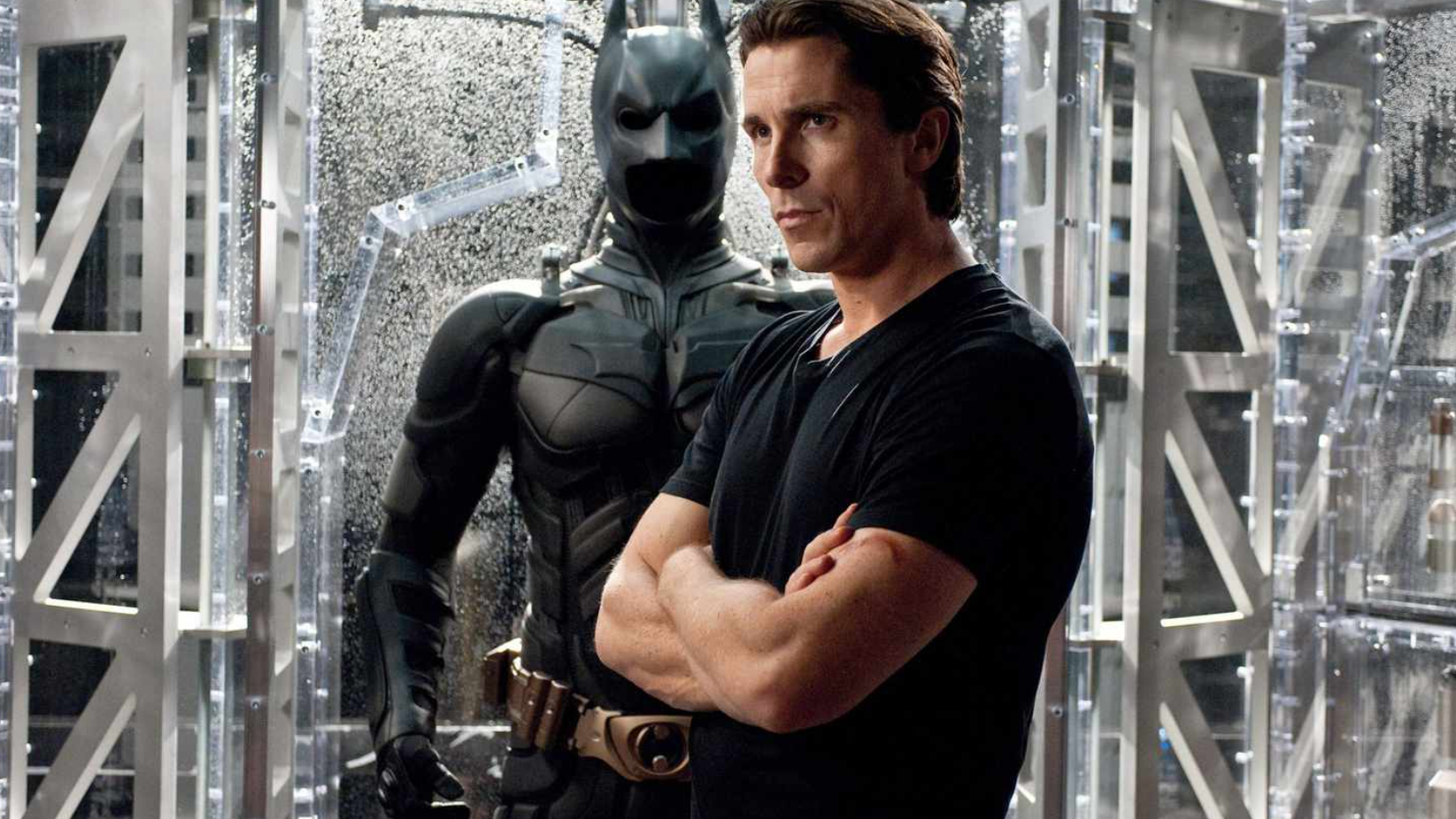 Christian Bale as Bruce Wayne standing in front of the Batsuit