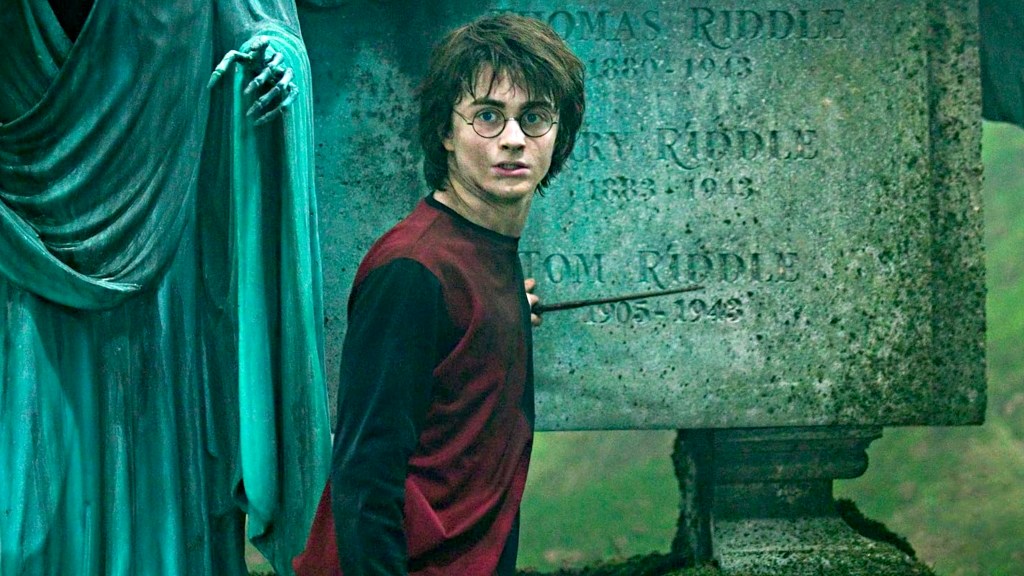 Daniel Radcliffe como Harry Potter sosteniendo una varita mágica frente a una estatua de piedra.