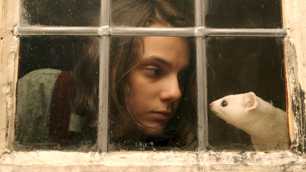 Dafne Keen and a pine marten through a window in His Dark Materials