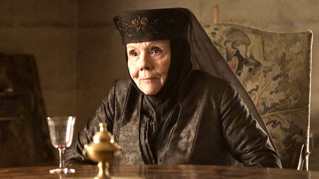 Diana Rigg como Olenna Tyrell sentada en una mesa de Juego de Tronos.