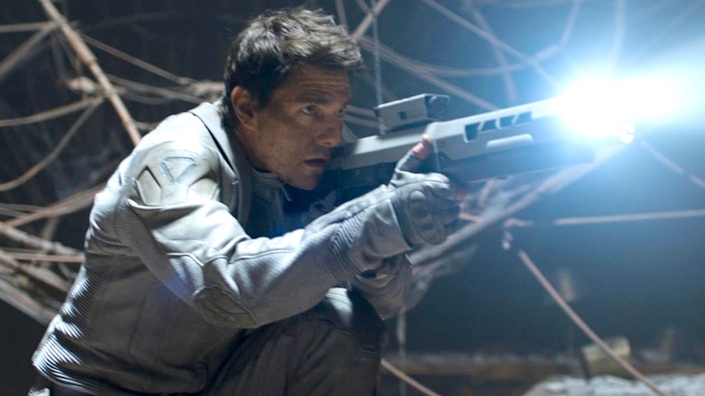 Tom Cruise wearing gray suit and gloves aiming rifle with flashlight attached in Oblivion