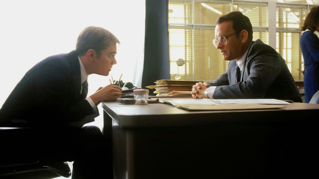 Leonardo DiCaprio and Tom Hanks sitting across from each other at a desk in Catch Me If You Can