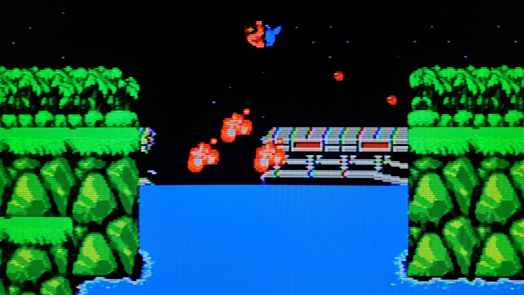 A screenshot from Konami on the Nintendo Entertainment System, showing the player jumping over an exploding bridge.