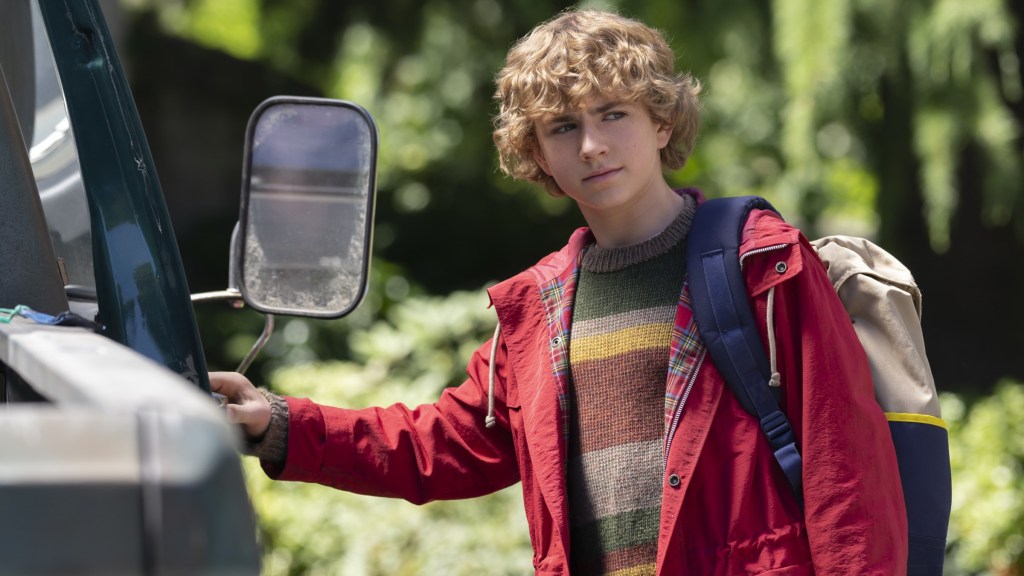 Walker Scobell as Percy Jackson wearing a red jacket and opening the door of a truck in Percy Jackson & the Olympians