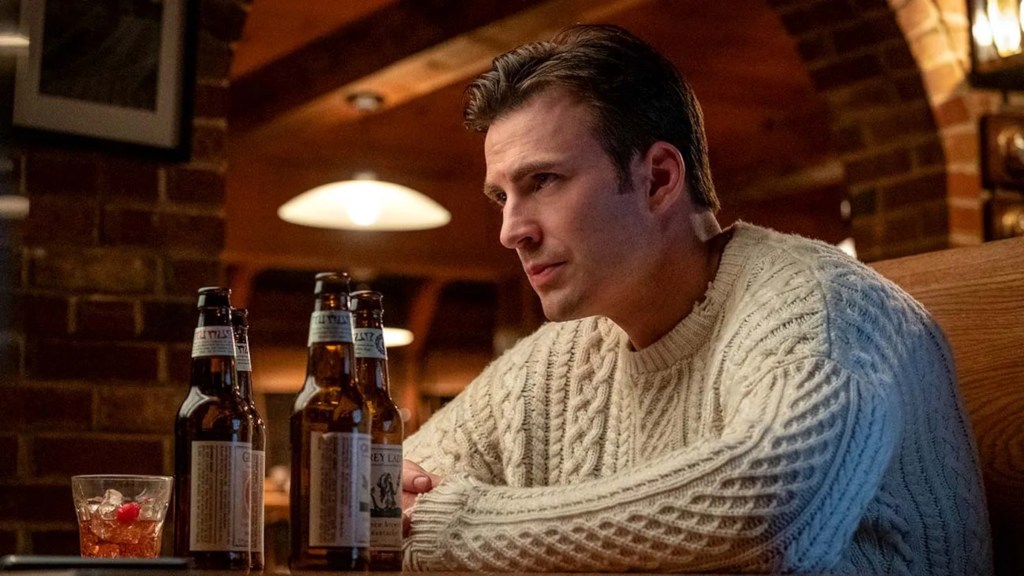 Chris Evans as Ransom Dysdale wearing a white sweater and sitting at a bar table in Knives Out