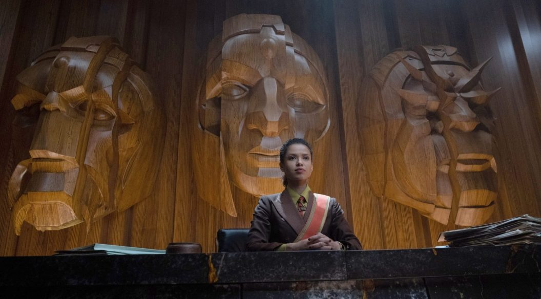 A woman sitting at a desk with huge heads on the wall behind her.